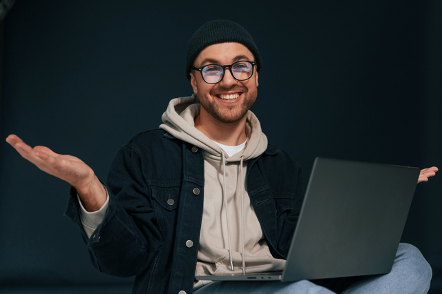Smiling, sitting and using laptop. Handsome man is in the studio against background.